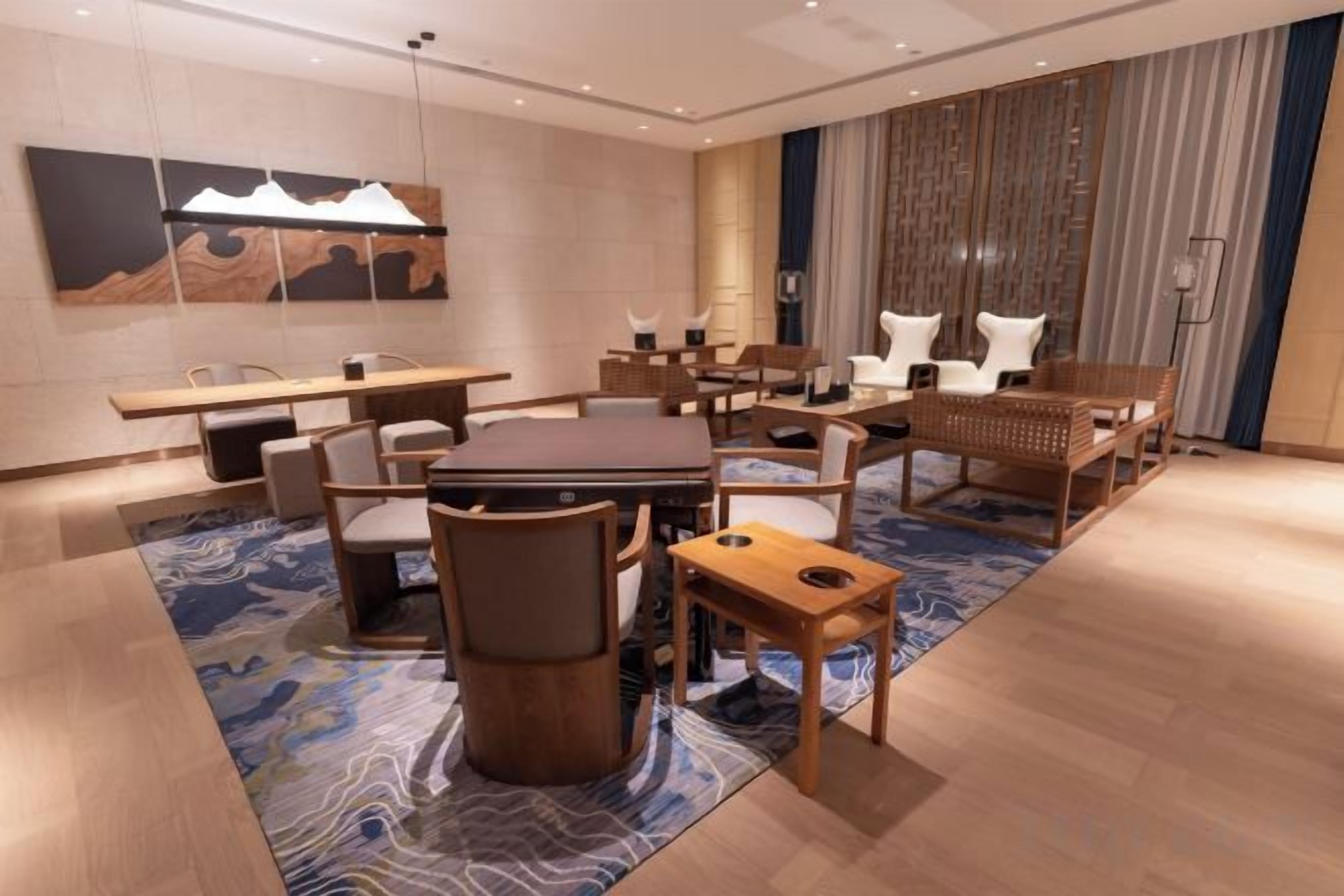 A modern hotel room with a dining area, a large painting on the wall, and a patterned rug.