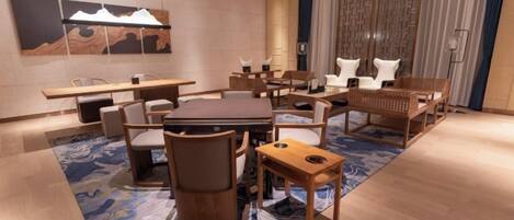 A modern hotel room with a dining area, a large painting on the wall, and a patterned rug.