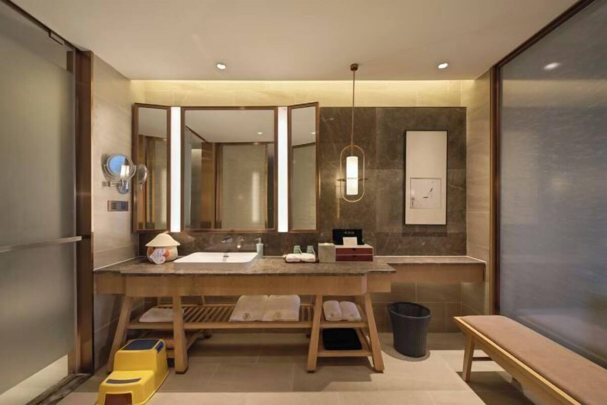 A modern bathroom with a large mirror, dual sinks, and a bench.