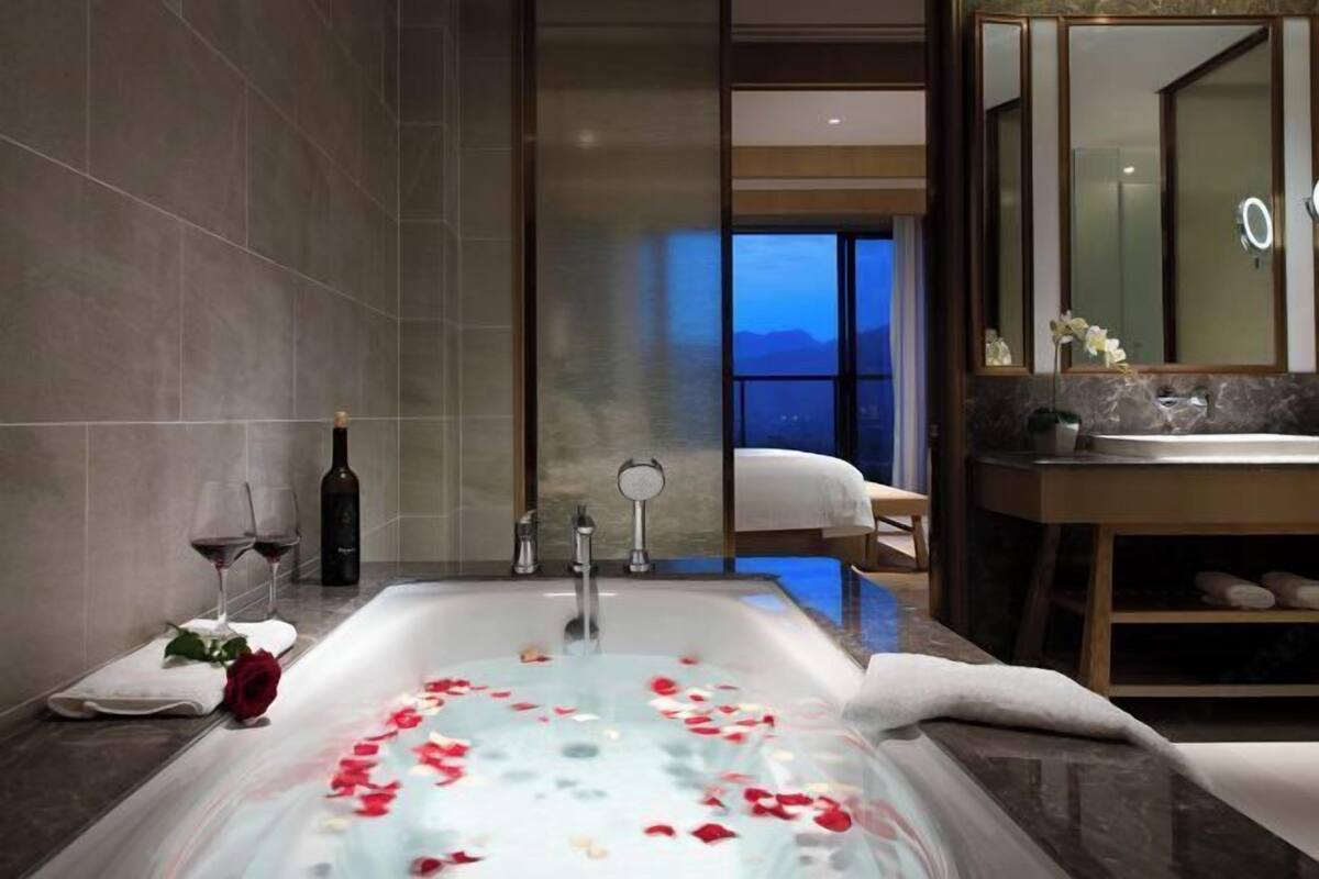 Een moderne badkamer met een bad, een spiegel en uitzicht op een slaapkamer.