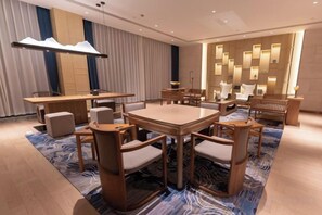 A hotel room with a large dining table, multiple chairs, a sofa, and a patterned carpet.