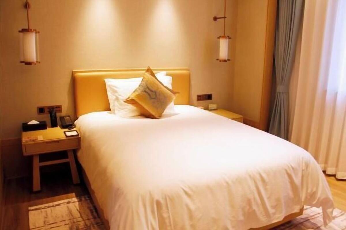 Een hotelkamer met een bed, nachtkastjes, lampen en gordijnen.