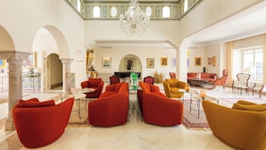 A spacious lobby with a high ceiling, ornate ceiling design, and a chandelier. There are multiple seating areas with red and mustard-colored sofas. - Nawara Residence (La Marsa)