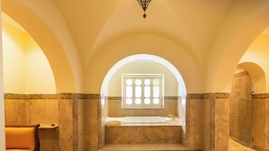 A bathroom with a large bathtub, a bench, and a window with a view. - Nawara Residence (La Marsa)