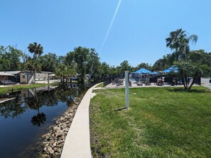 Enjoy a serene riverside setting with a pathway along the water's edge, featuring a pool and lounge chairs.