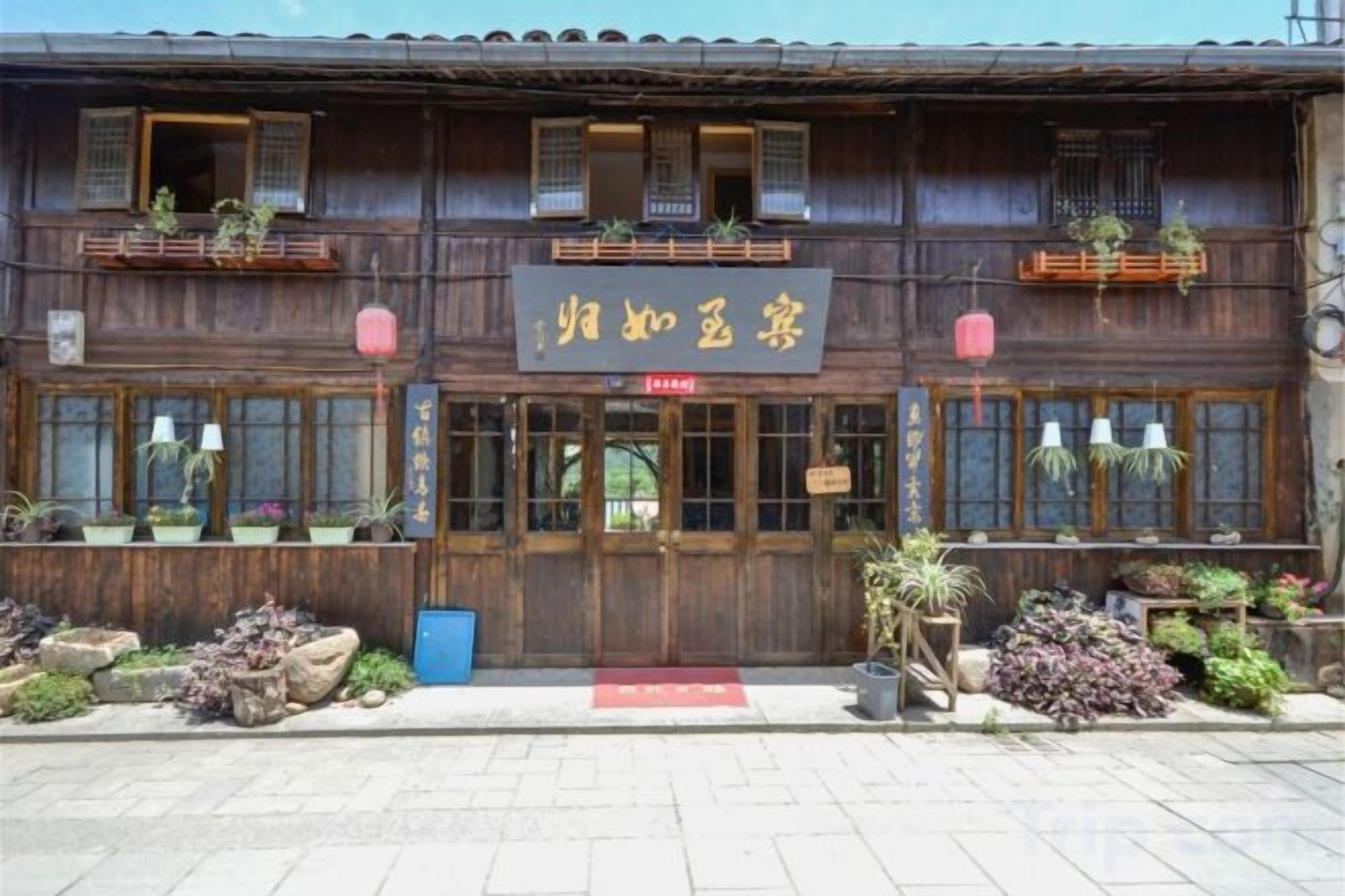 A traditional wooden building with a signboard, windows, and potted plants.