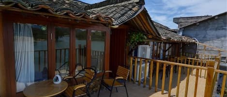 A traditional Japanese-style building with a wooden deck, outdoor seating, and a thatched roof.