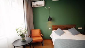 A hotel room with a bed, a chair, a small table, a potted plant, and an air conditioning unit. - Guyan Huaxiang Jiangnan Hostel (Lishui)