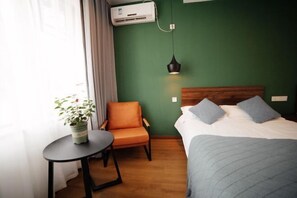 A hotel room with a bed, a chair, a small table, a potted plant, and an air conditioning unit. - Guyan Huaxiang Jiangnan Hostel (Lishui)