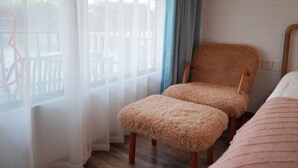 A room with a wooden chair and ottoman, a bed, and a view through a window with sheer curtains. - Guyan Huaxiang Jiangnan Hostel (Lishui)