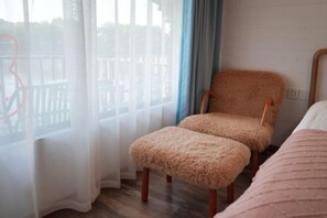 A room with a wooden chair and ottoman, a bed, and a view through a window with sheer curtains. - Guyan Huaxiang Jiangnan Hostel (Lishui)