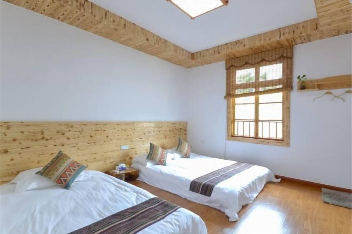 Una stanza con due letti, travi in legno a soffitto, una finestra con persiane e uno scaffale con una pianta.