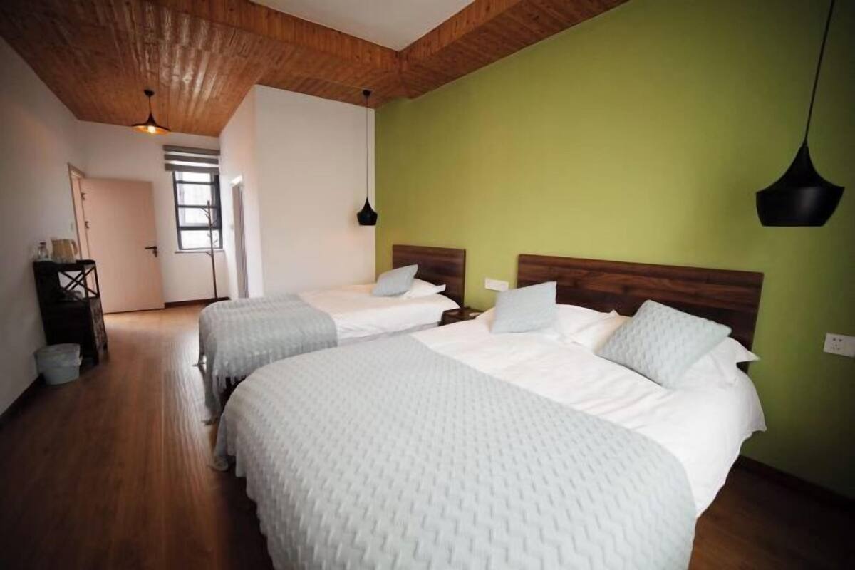 Una stanza con due letti, travi a vista in legno, una parete verde e una finestra.