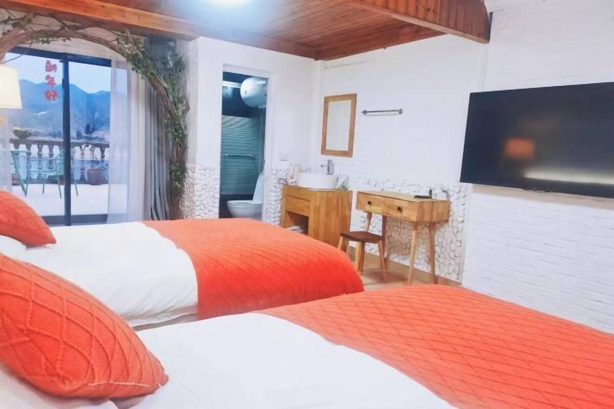 Una camera da letto con due letti, una cassettiera in legno, una televisione e una finestra con vista sulle montagne.