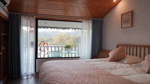 A bedroom with a large bed, a balcony with a table and chairs, and a view of trees and mountains. - Guyan Huaxiang Jiangnan Hostel (Lishui)