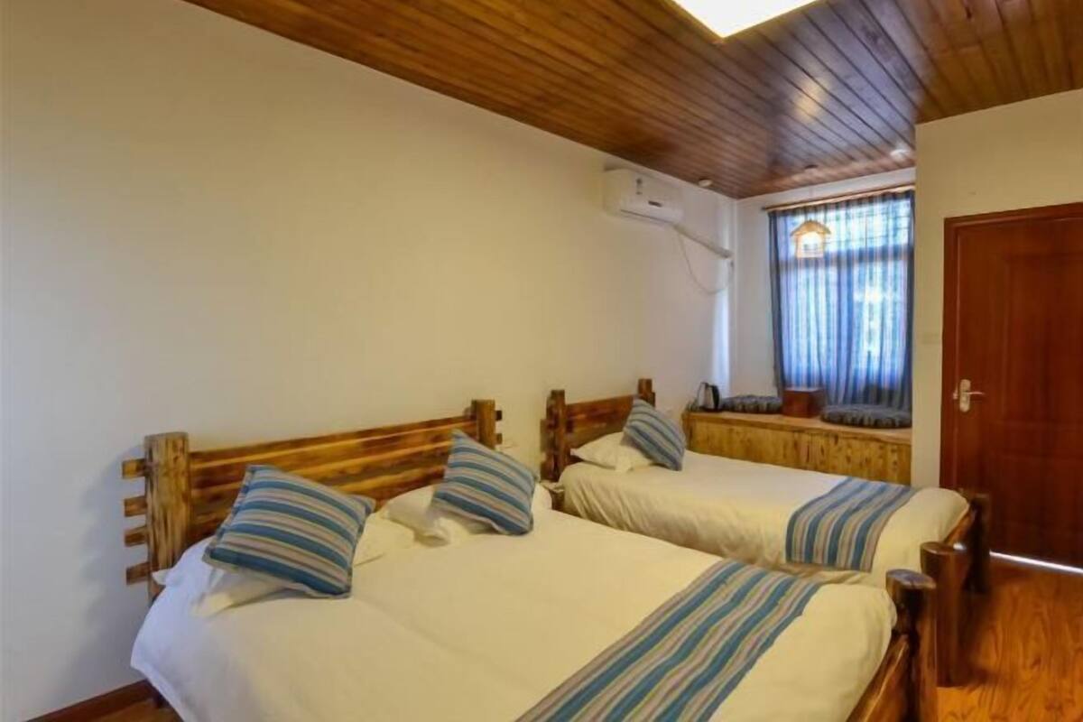 Una stanza con due letti in legno, biancheria da letto bianca, cuscini a righe e un soffitto in legno, oltre a una finestra con tende.