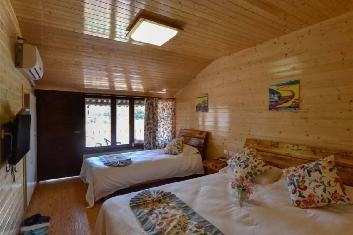 Una baita in legno con due letti, una televisione e una finestra con tende.