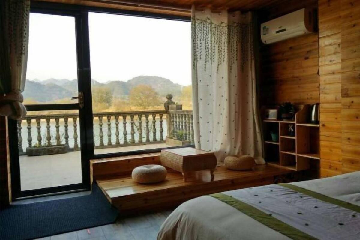 Una camera con un letto, un piccolo tavolo, una panca, uno scaffale e vista sulle montagne dal balcone.