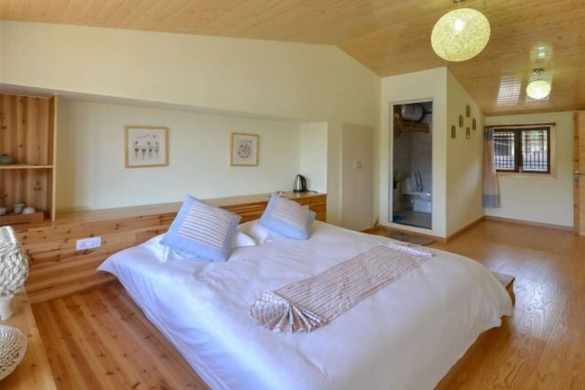 Una camera accogliente con pavimento in legno, un letto grande con biancheria bianca, un comodino e una lampada a sospensione.