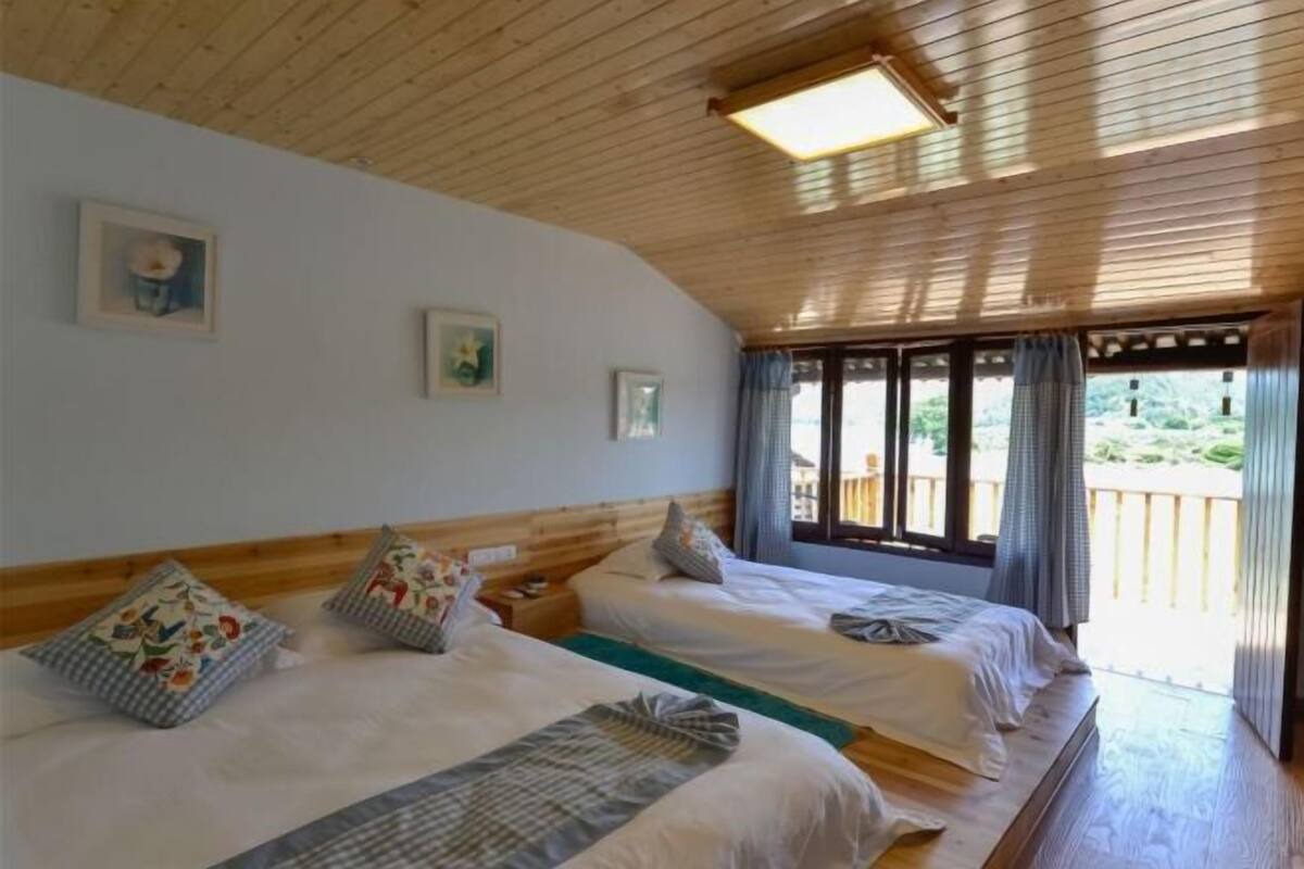 Una stanza con due letti, soffitto in legno e vista sul verde.