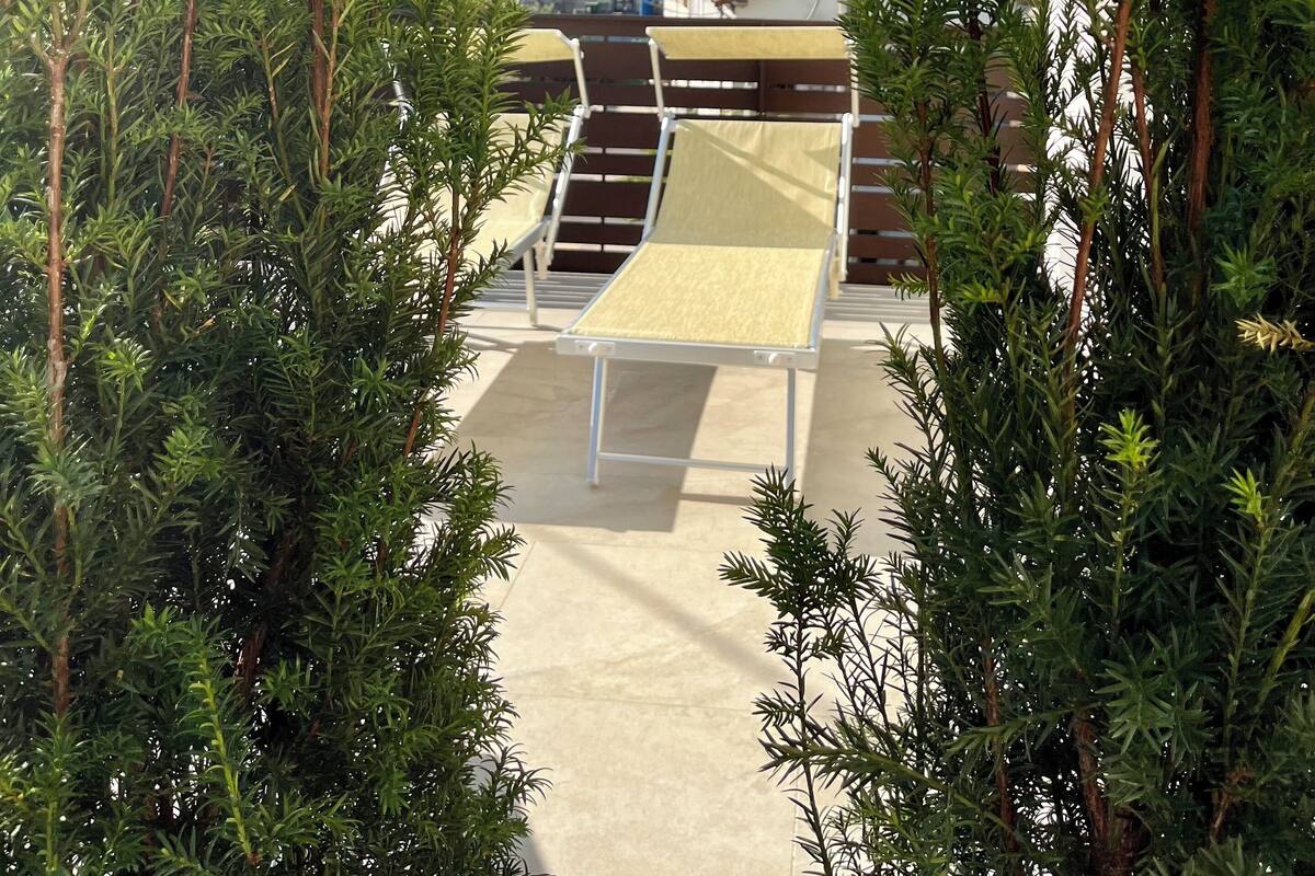 Un espace extérieur abrité, doté d’une table de billard, entouré d’arbres à feuilles persistantes, et offrant une vue sur des bâtiments et des collines en arrière-plan.