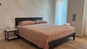 A bedroom with a bed, a nightstand, a lamp, a wardrobe, and a window with curtains.