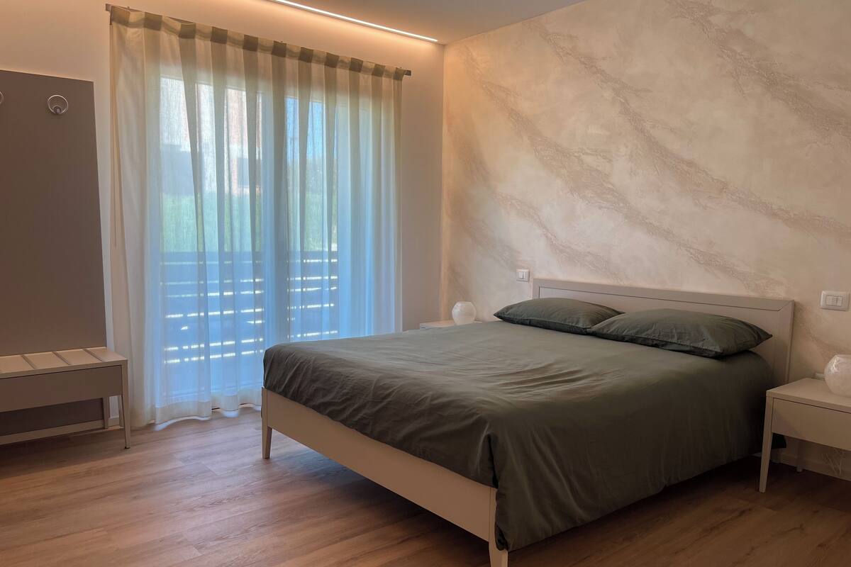 Une chambre à coucher moderne, avec un lit, des tables de chevet et une fenêtre ornée de rideaux légers.