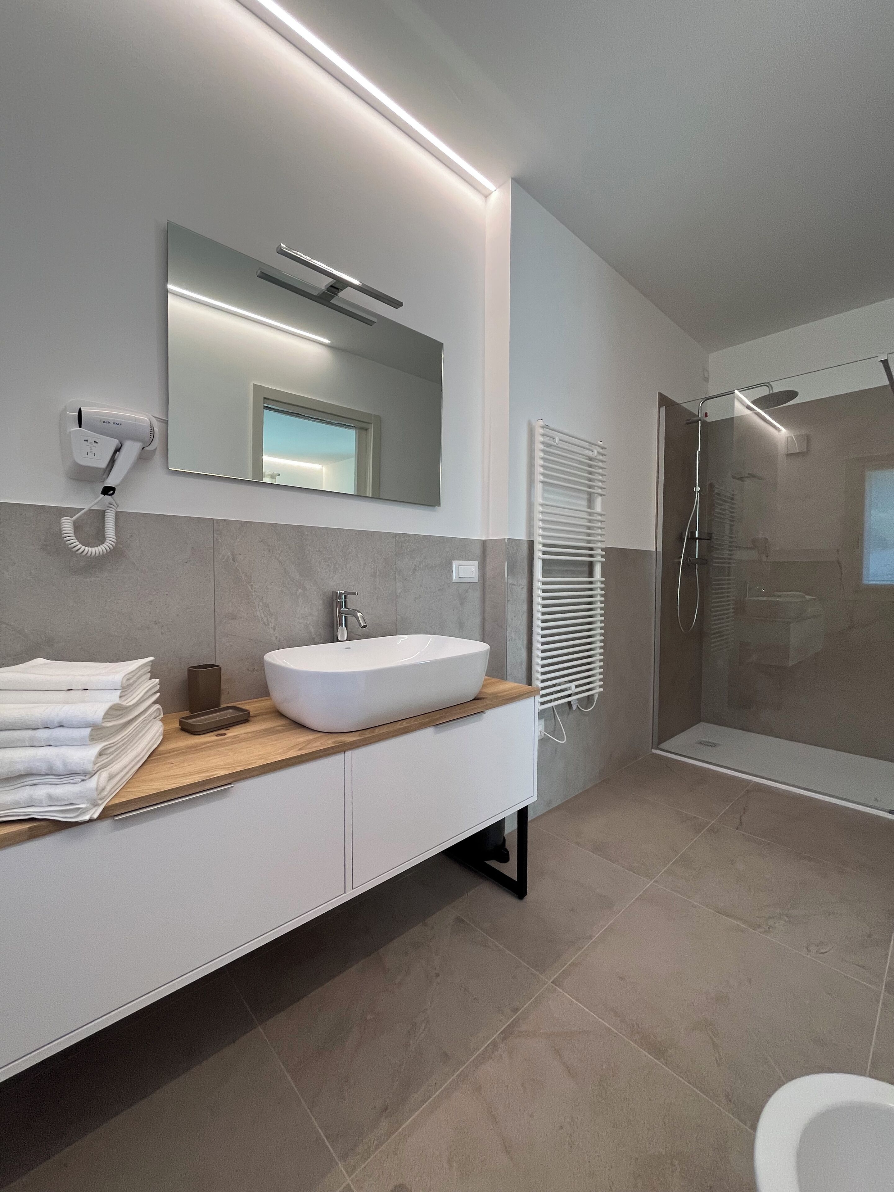 Een moderne badkamer met een groot wastafel, een spiegel, een haardroger en een douche.