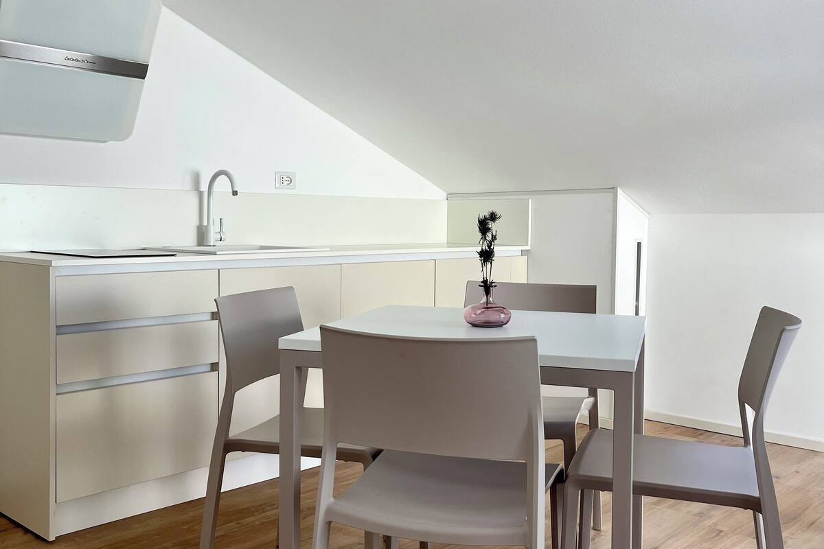 Une cuisine moderne avec des meubles blancs, un four encastré et un coin repas comprenant une table ronde et quatre chaises.