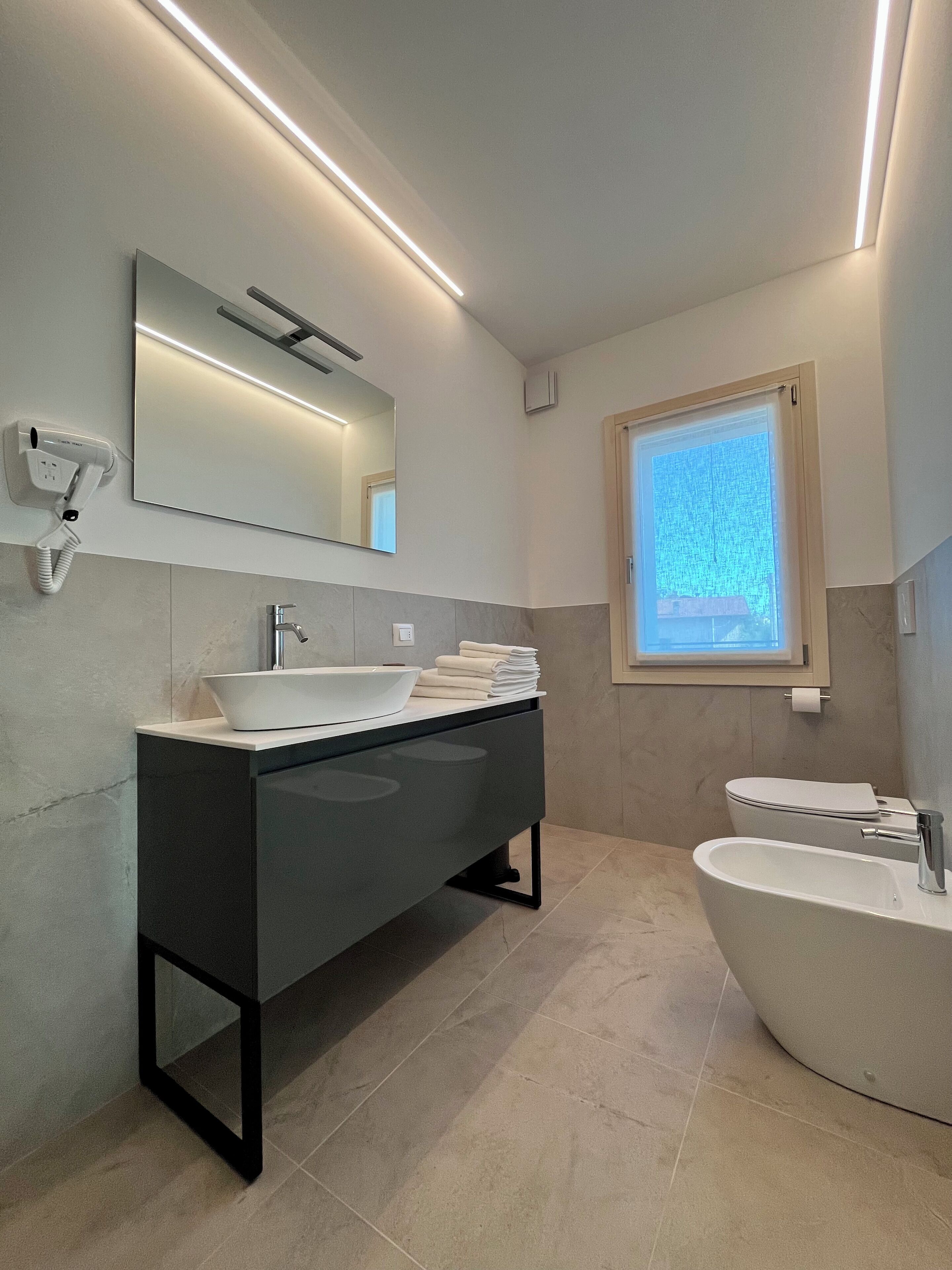 Un baño moderno con un amplio tocador, una bañera independiente, un espejo y una ventana.