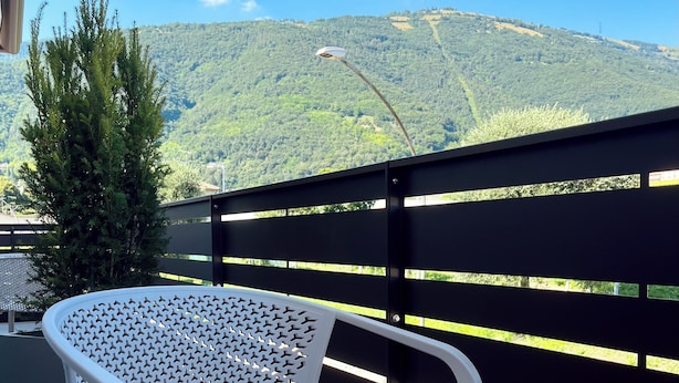 A white perforated chair on a balcony with a view of green hills and a clear sky. - Alle Colline (Valdobbiadene)