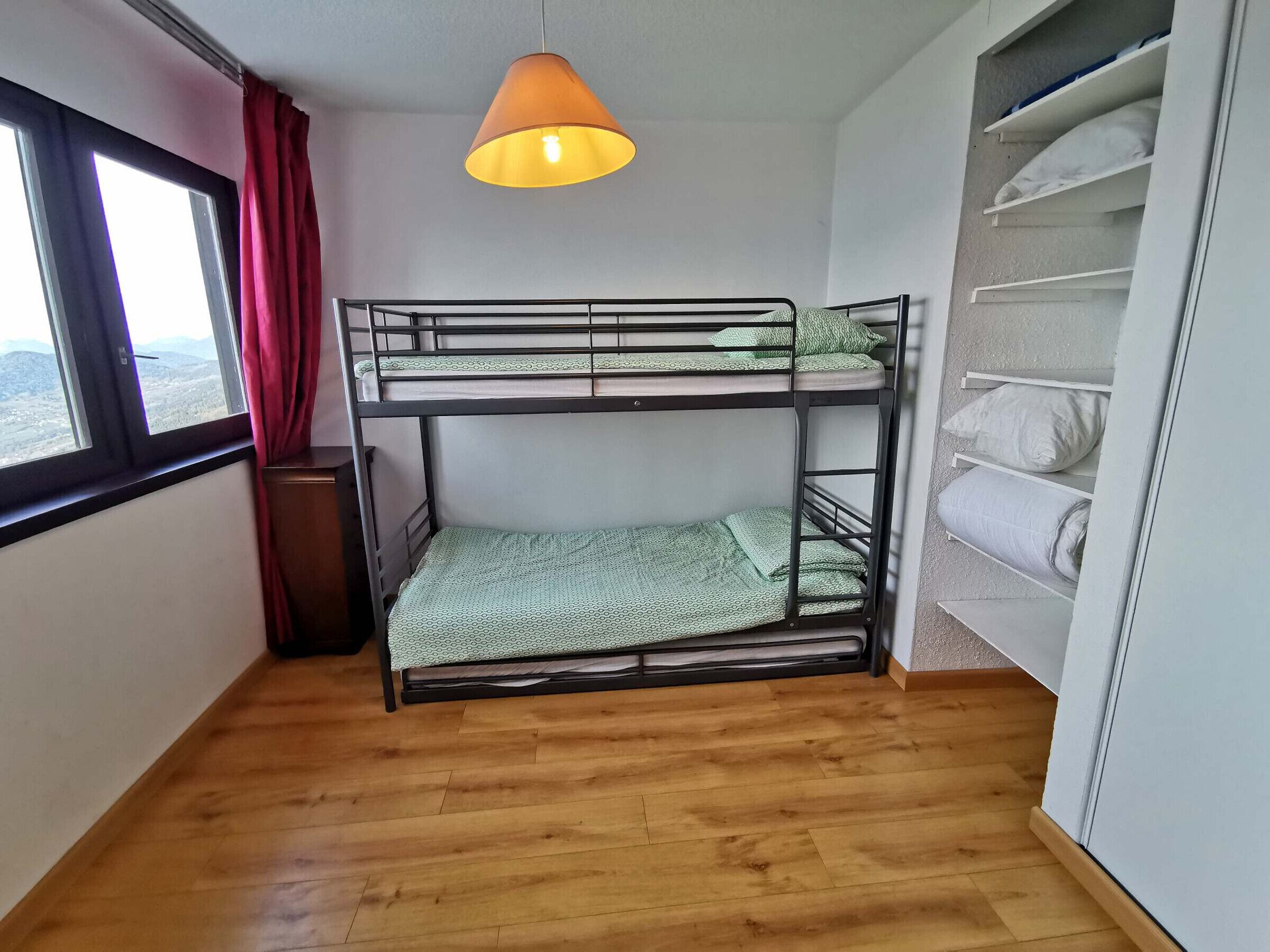 A bunk bed room with a window, a hanging lamp, and a shelf with folded blankets.