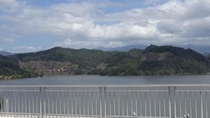 A view of a lake with mountains in the background, a metal railing in the foreground, and a partly cloudy sky. - Taining Luxiang Nanhui Hotel (Jinhu Prairie) (Taining)