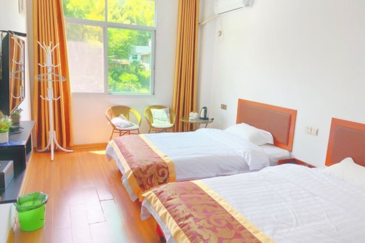 Habitación de hotel con dos camas, un escritorio, una silla, una ventana con cortinas y vistas a zonas verdes.