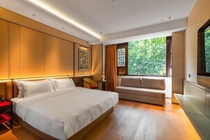 Habitación de hotel moderna con una cama grande, un sofá, un televisor y una ventana con vistas a zonas verdes.