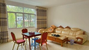 A living room with a beige sofa, red and blue chairs, a wooden coffee table, and a window with curtains. - Taining Luxiang Nanhui Hotel (Jinhu Prairie) (Taining)