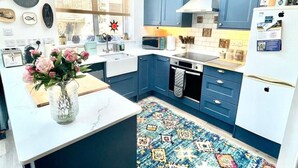 Una cocina moderna con armarios azules, encimeras blancas y diversos electrodomésticos, incluyendo un microondas, estufa y refrigerador.