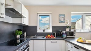 A modern kitchen with a stove, oven, sink, and microwave. There is a window with a view of the sky and a clock on the wall. - Hansekogge - detached, first row on the water, sauna, whirlpool tub, shower (Olpenitz)