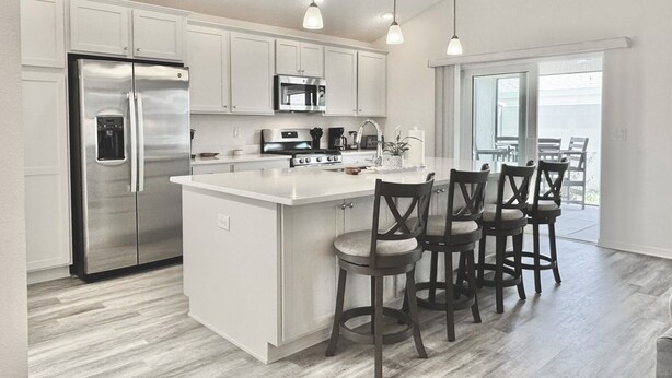 A modern kitchen with white cabinetry, stainless steel appliances, and a central island with bar stools. - Lost Shaker of Salt - 3/3 w/ 4-Seater Golf Cart in Moultrie Creek, The Villages! (The Villages)