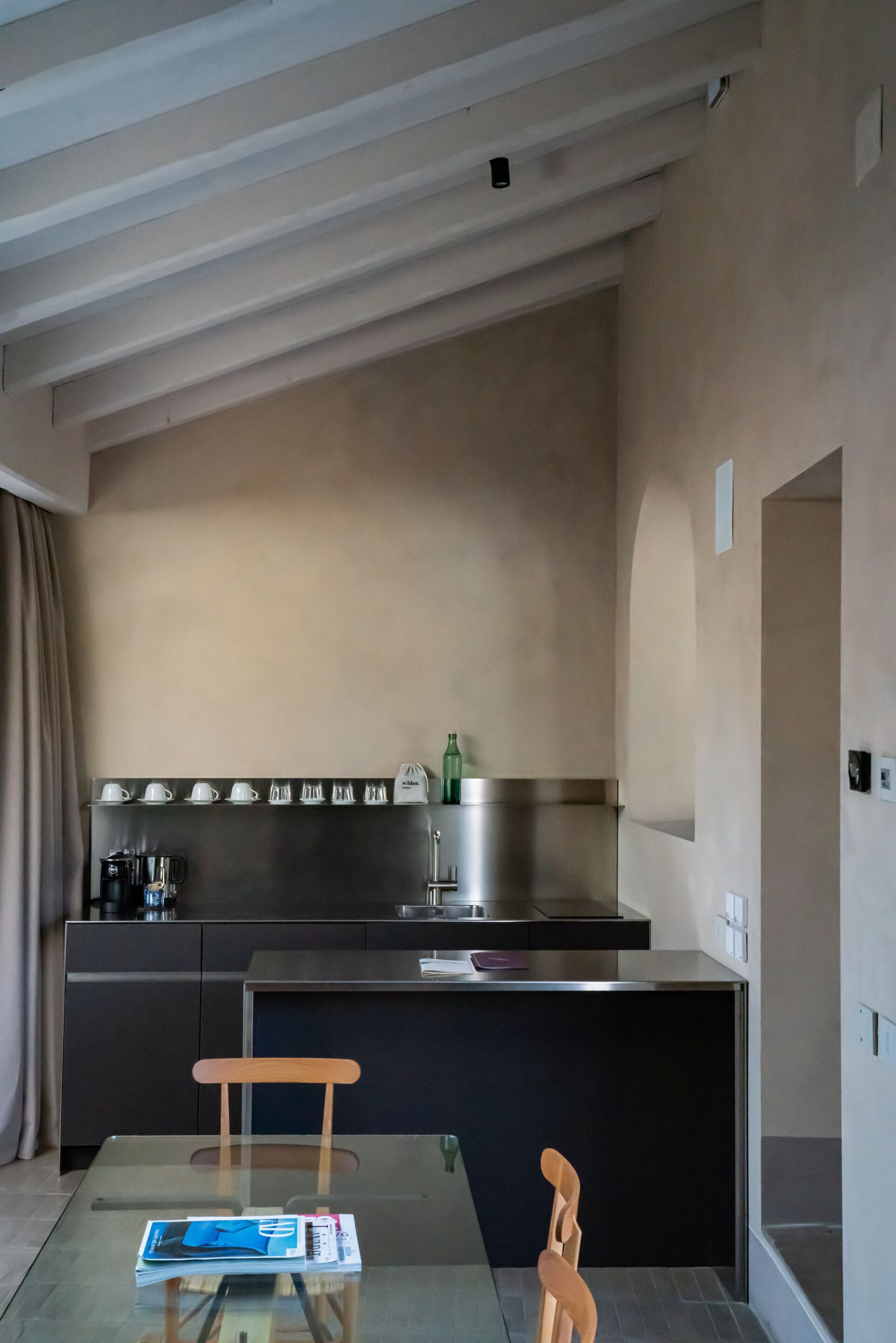 Eine moderne Küche mit einem Glastisch, einem Holzsessel und einer Kücheninsel mit Dunstabzugshaube aus Edelstahl.