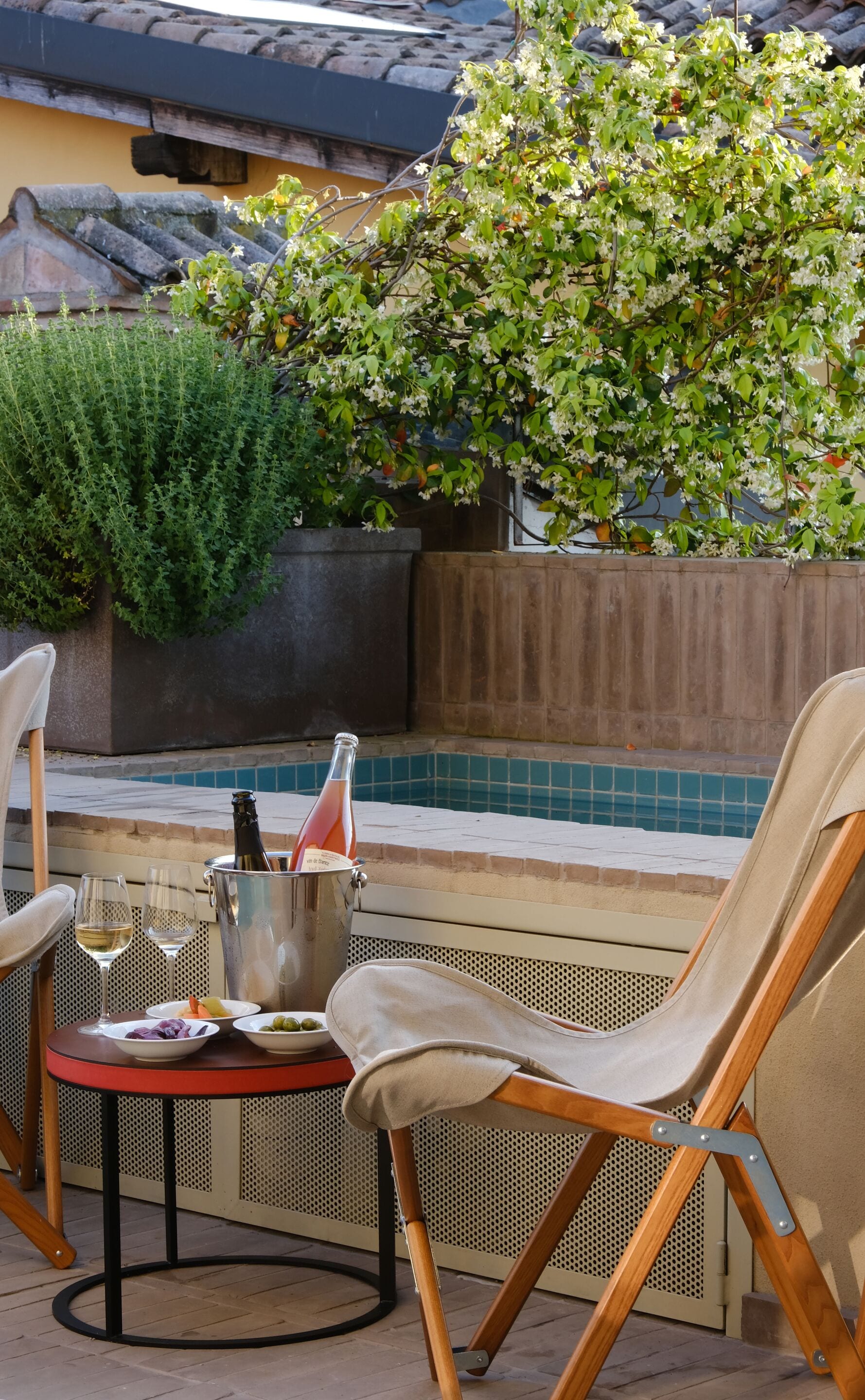 An outdoor seating area with a table, chairs, a bottle of wine, and a pool in the background.