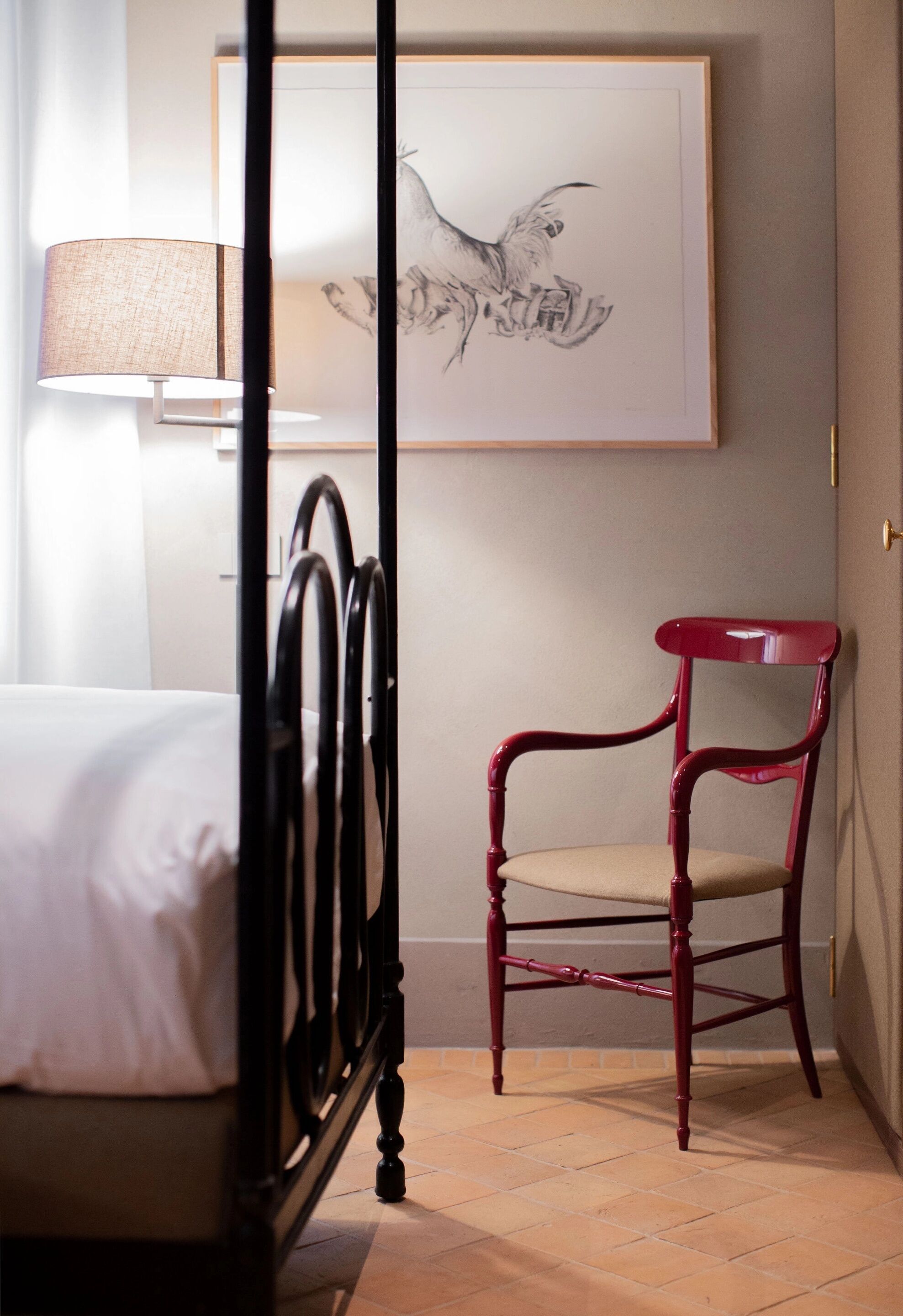 A bedroom with a four-poster bed, a red chair, and a framed artwork on the wall.