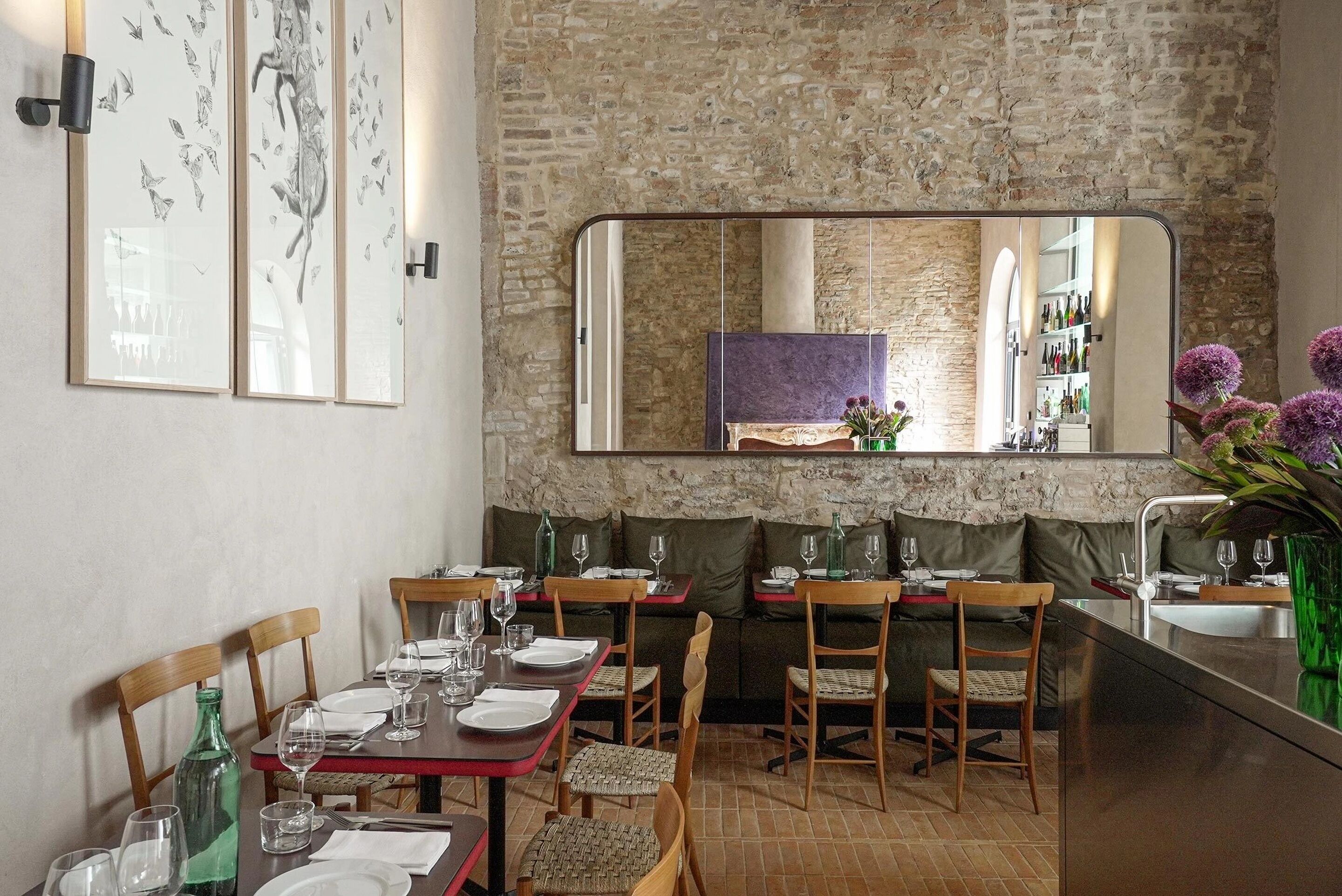 Un espace repas avec des tables et des chaises en bois, un mur en briques et un grand miroir qui reflète la pièce.