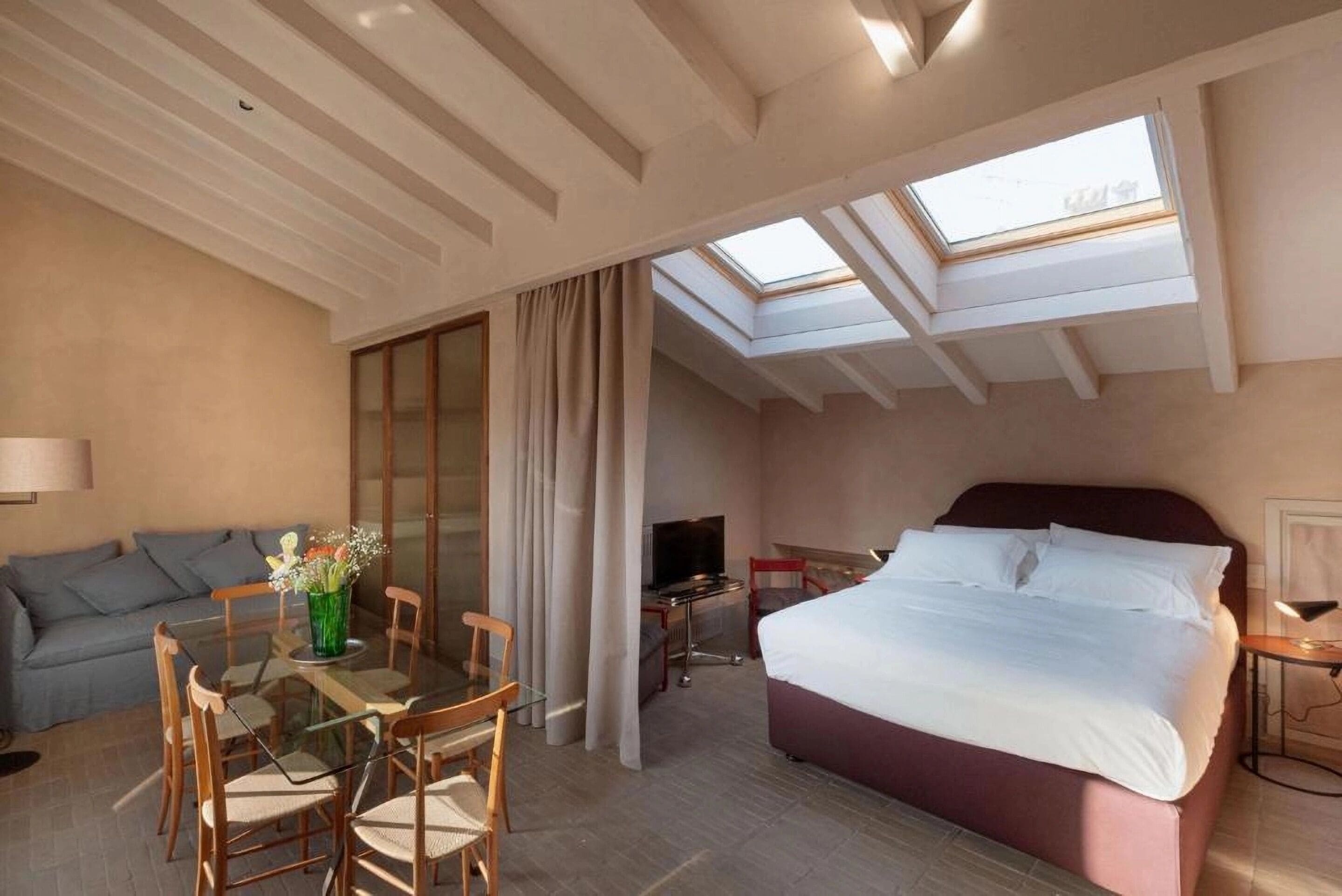 A hotel room with a bed, a TV, a glass dining table, and a sofa.