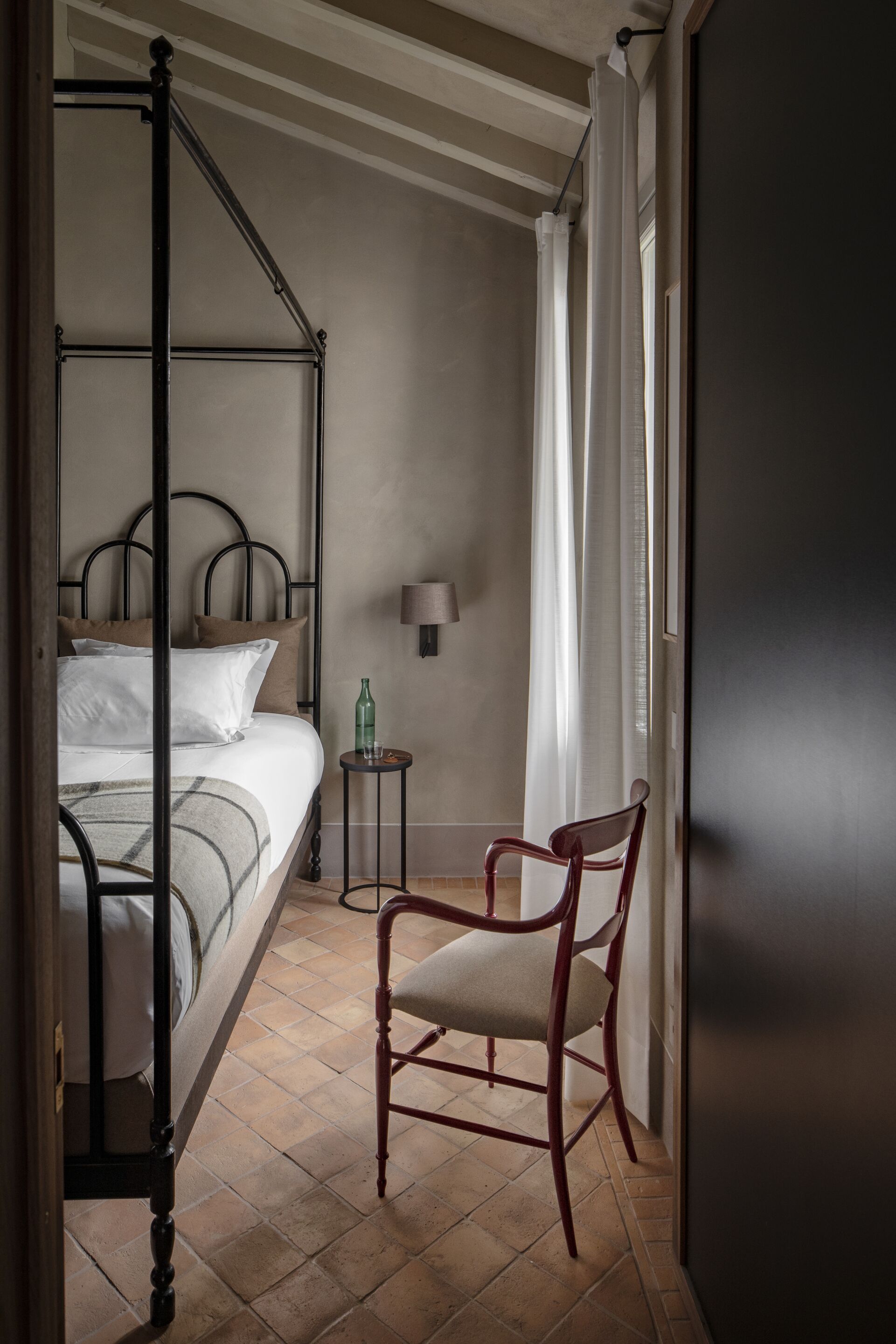 Un dormitorio con una cama con dosel, una silla, una mesita y una lámpara.