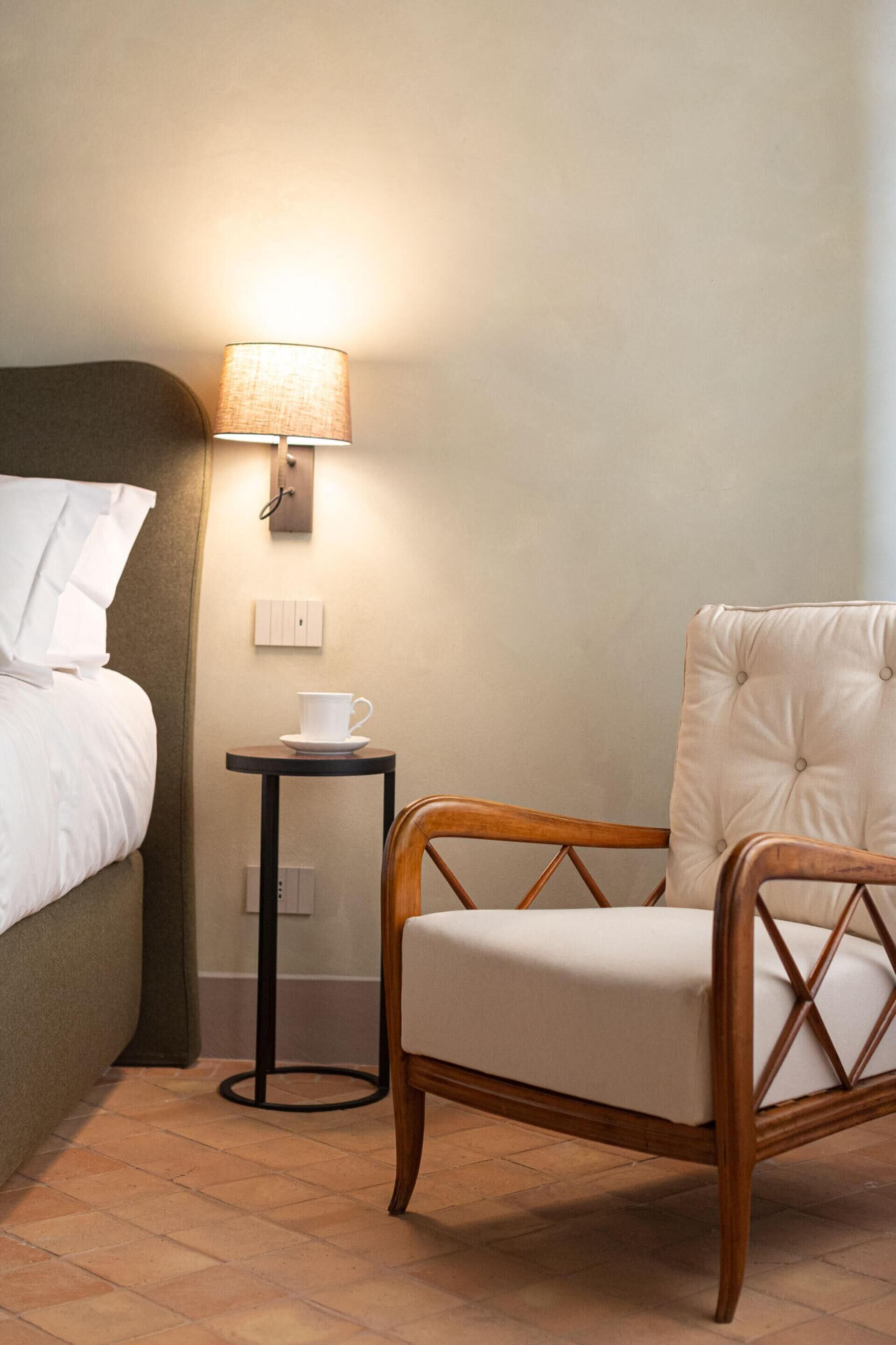 Une chambre d’hôtel avec un lit, une petite table sur laquelle se trouve une tasse, une chaise et une lampe fixée au mur.