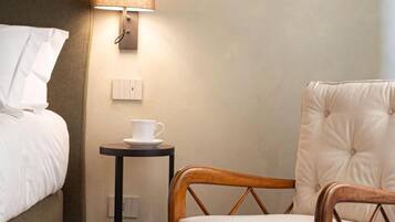 Une chambre d’hôtel avec un lit, une petite table sur laquelle se trouve une tasse, une chaise et une lampe fixée au mur.