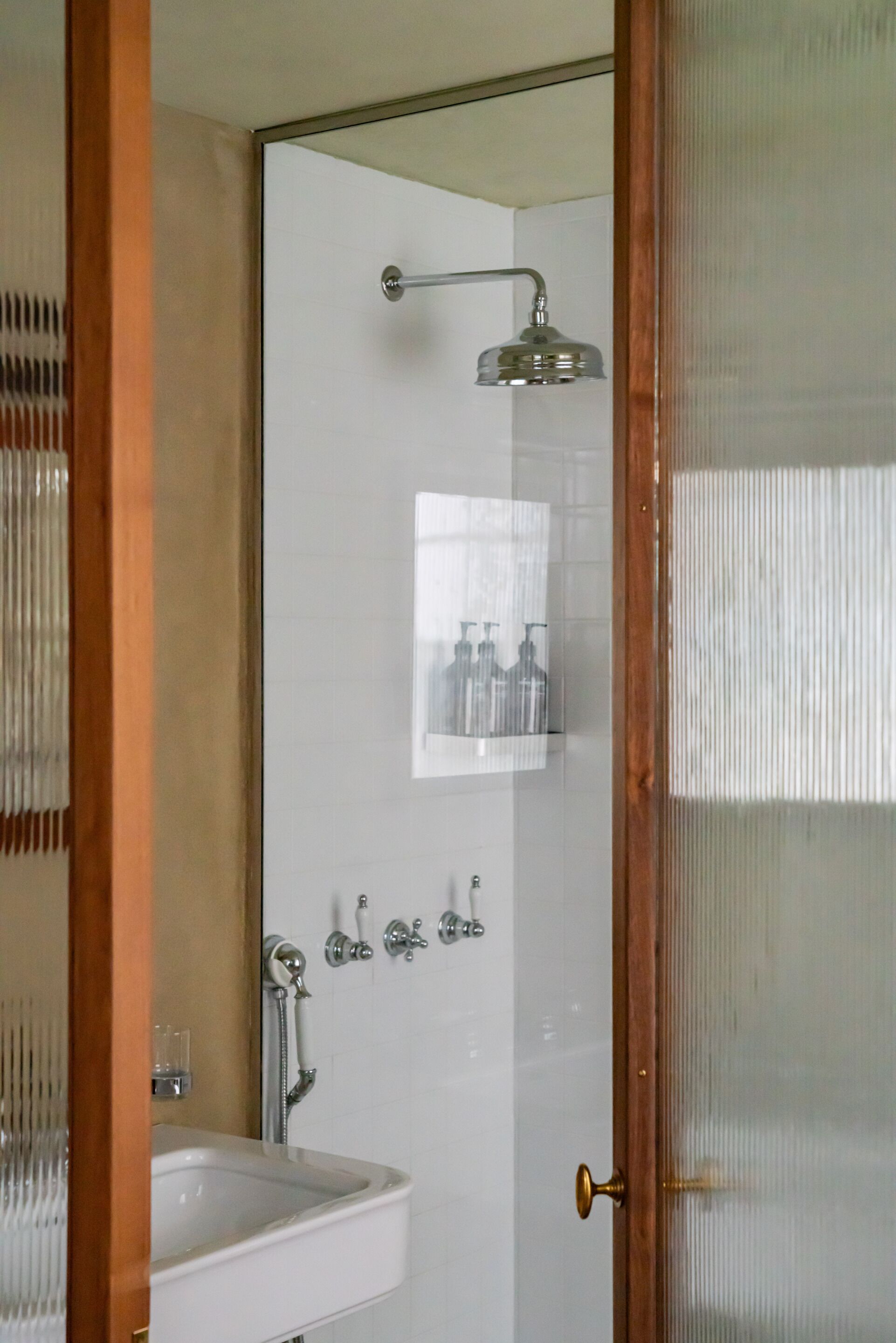 Ein Badezimmer mit einem weißen Waschbecken, einer Dusche mit Duschbrausehandstück und einer Duschkabine mit Messinggriff.