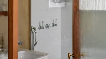 Casa de banho com lavatório branco, chuveiro com duche manual e porta de vidro com puxador de latão.