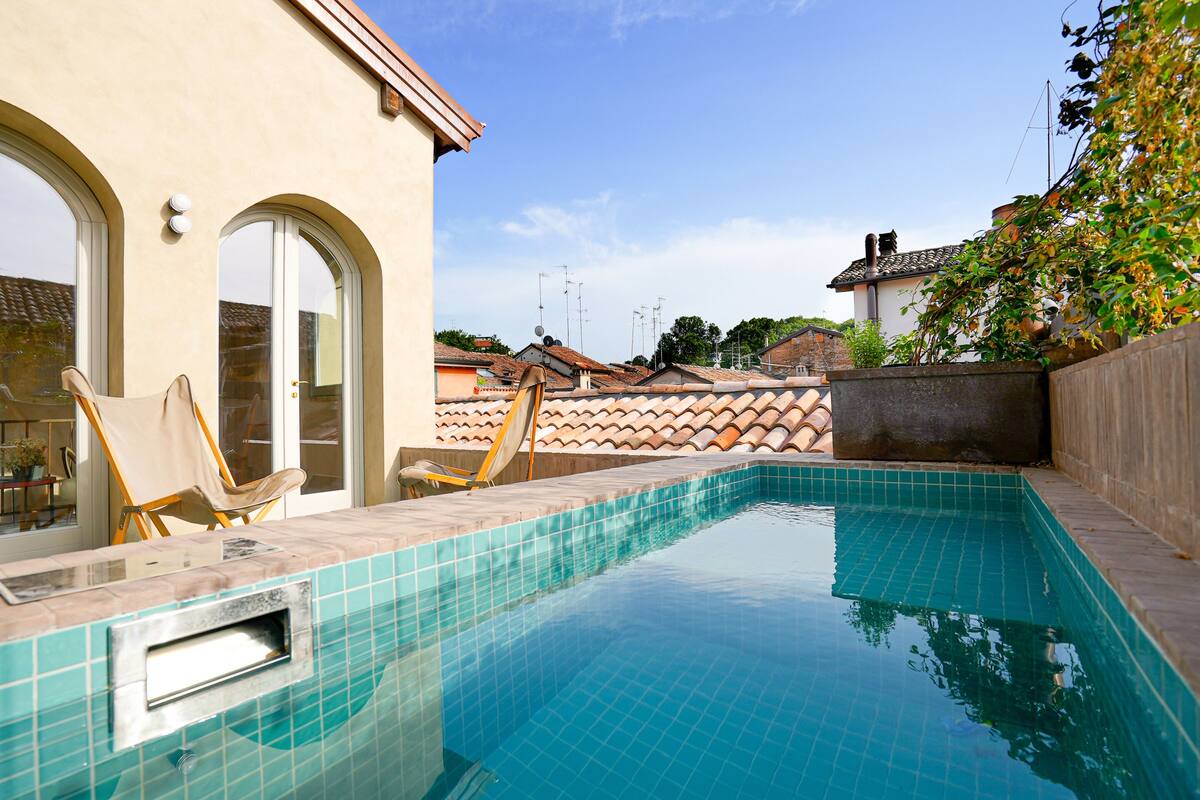 A swimming pool with tiled edges, a chair, and a wall with a tiled roof.